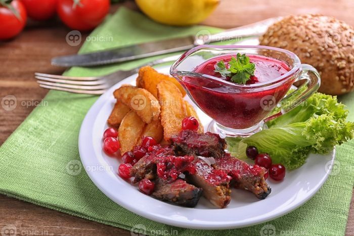 دانلود گوشت گاو با سس گوجه فرنگی، سیب زمینی سرخ شده بر روی بشقاب، روی زمینه چوبی