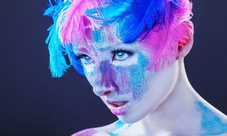 دانلود یک زن جوان جذاب با آرایش با پرهای رنگارنگ روشن در پس زمینه تاریک