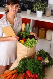 دانلود زن جوان نگه داشتن سبد خرید مواد غذایی با سبزیجات در آشپزخانه ایستاده