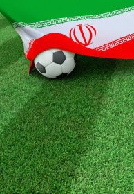 دانلود توپ فوتبال و پرچم ملی ایران بر روی چمن سبز قرار دارد