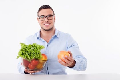 دانلود مرد خوش تیپ برگه میوه ها و سبزیجات را نگه می دارد. او به دوربین به رنگ نارنجی نشان می دهد