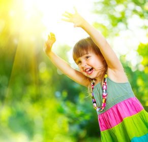 دانلود دختر کوچولو خوش شانسی سرگرم کننده در خارج از منزل. زیبا و سالم 3 ساله کودک خنده و بالا بردن دست، بازی کردن و لبخند در پارک تابستانی