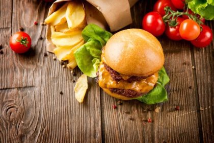 دانلود همبرگر با سیب زمینی سرخ شده روی میز چوبی. Cheeseburger در نان تازه با پیت گوشت گاو شکری و مواد غذایی تازه سالاد خدمت کرده است