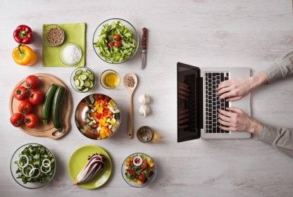 دانلود مردی در آشپزخانه در جستجوی دستور العمل های موجود در لپ تاپ خود با مواد غذایی و سبزیجات تازه در نمای چپ و چپ