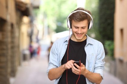 دانلود پسر خوشحال راه رفتن و استفاده از تلفن هوشمند برای گوش دادن به موسیقی با هدفون