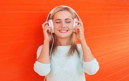 دانلود زن جوان جوان موسیقی را در هدفون در برابر دیوار رنگی نارنجی گوش می دهد و از آن لذت می برد