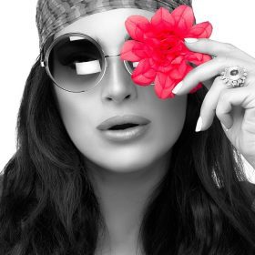 دانلود پرتره تک رنگ یک زن جوان شیک ، با عینک گرد مد روز با گل های صورتی در چشم خود پوشیده و به دوربین نگاه می کند