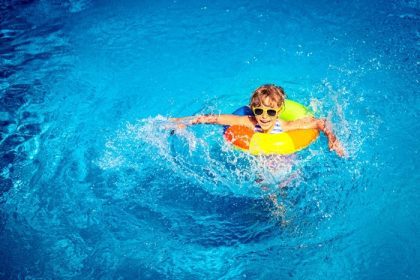 دانلود کودک خوشحال در استخر شنا بازی می کند. مفهوم تعطیلات تابستانی. نمای عمودی