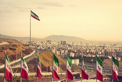 دانلود مجموعه پرچم های ایران در مقابل افق تهران و یک پرچم بزرگ در پس زمینه در غروب خورشید با رنگ نارنجی گرم