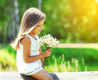 دانلود پرتره کودک دختر ناز با دسته گل های گل بابونه در روز تابستانی آفتابی
