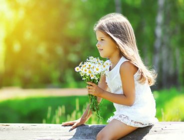 دانلود پرتره دختر بچه ناز با دسته گل های گل بابونه در روز تابستانی آفتابی