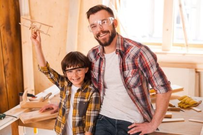 دانلود سازندگان رویایی. پسر بچه ای شاد که هنگام کار با پدرش در کارگاه ، هواپیمای چوبی دارد