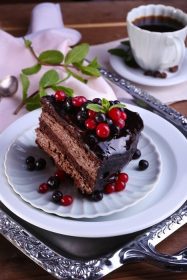 دانلود کیک شکلاتی خوشمزه با انواع توت ها و فنجان قهوه روی میز نزدیک است