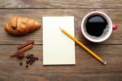 دانلود فنجان قهوه با کروسانت تازه و ورق کاغذ خالی روی میز چوبی ، نمای بالا