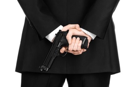دانلود سلاح گرم و موضوع امنیتی مردی با کت و شلوار مشکی است که اسلحه ای را روی زمینه سفید جدا شده در استودیو نگه داشته است