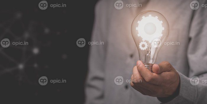 دانلود عکس دست یک مرد تاجر یک لامپ در دست دارد و یک نماد چرخ دنده دارد
