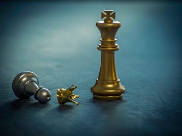 دانلود عکس مهره شطرنج نقره ای تاج طلا می پوشد که روی صفحه شطرنج ایستاده است