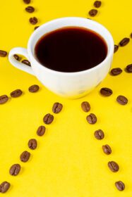 دانلود عکس یک فنجان قهوه تازه روی پس زمینه زرد و دانه های قهوه