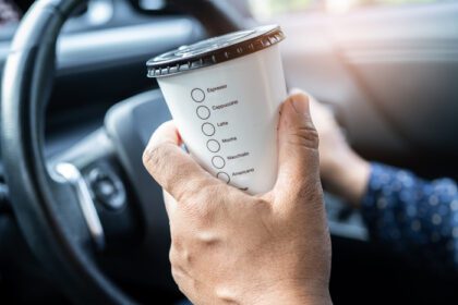 دانلود عکس بانوی آسیایی که غذای داغ فنجان قهوه را برای نوشیدن در ماشین نگه می دارد