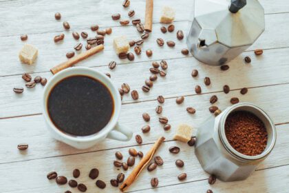 دانلود عکس دانه های قهوه و فنجان قهوه روی میز در پس زمینه