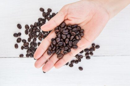 دانلود عکس دانه های قهوه در دست در مقابل پس زمینه قهوه