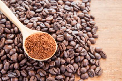 دانلود عکس پودر قهوه در قاشق چوبی و دانه های قهوه روی میز چوبی