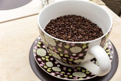 دانلود عکس دانه قهوه در یک لیوان سرامیکی بزرگ در پس زمینه میز