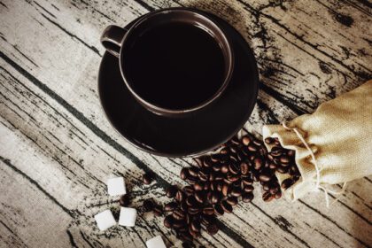 دانلود عکس فنجان قهوه با دانه های روی میز چوبی پارچه کتان