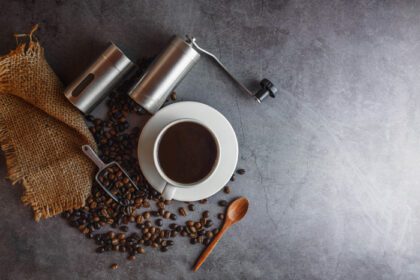 دانلود عکس آسیاب قهوه دستی و دانه های قهوه و فنجان قهوه روی میز