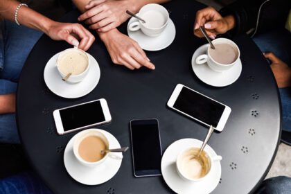 دانلود عکس دست با فنجان قهوه و گوشی هوشمند در یک کافه شهری