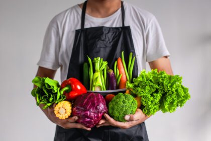 دانلود عکس مردی که پیش بند پوشیده است و سبزیجات مختلف را در هر دو دست گرفته است