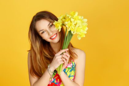 دانلود عکس زنی که گل های زرد در دست دارد و به دیوار زرد لبخند می زند