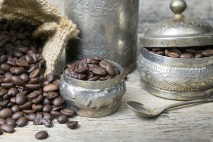 دانلود عکس فنجان نقره و دانه های قهوه در کیسه گونی روی چوب