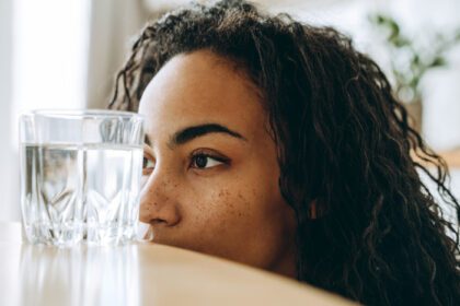 دانلود عکس زن جوان سیاهپوست در حالی که نشسته به لیوان آب نگاه می کند