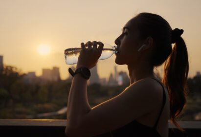 دانلود عکس زن جوان در حال نوشیدن آب بعد از دویدن در هنگام غروب آفتاب