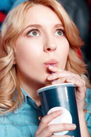 دانلود عکس زن جوان با شور و شوق در حال نوشیدن کوکا در سینما