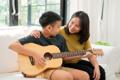 دانلود عکس مادر آسیایی در آغوش پسر پسر آسیایی در حال نواختن گیتار و