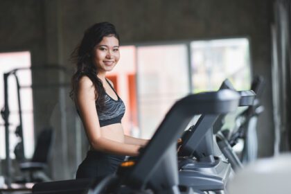 دانلود عکس زن ورزشکار آسیایی در حال دویدن روی تردمیل در باشگاه بدنسازی