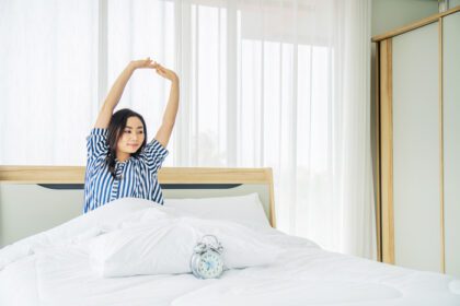 دانلود عکس زن جوان زیبا در حال کشش در رختخواب با دستانش بالا رفته