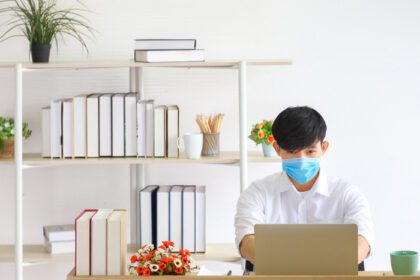 دانلود عکس کارمند مرد با پوشیدن ماسک صورت پزشکی که به تنهایی کار می کند