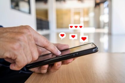 دانلود عکس دست مرد با استفاده از گوشی هوشمند با نماد قلب در دفتر او نگاه می کند