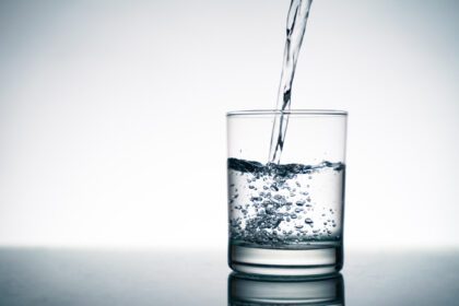 دانلود عکس نزدیک از ریختن آب شیرین در شیشه شفاف از بطری روی میز