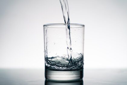 دانلود عکس نزدیک از ریختن آب شیرین در شیشه شفاف از بطری روی میز