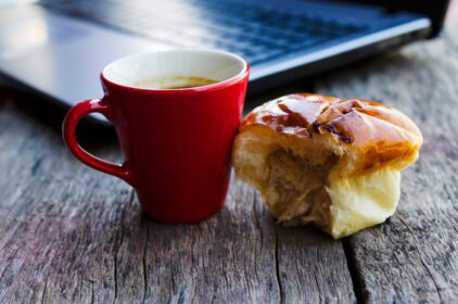 دانلود عکس فنجان قهوه قرمز و نان ماهی تن با لپ تاپ روی میز چوبی برای تکنولوژی سبک زندگی عشایر دیجیتال