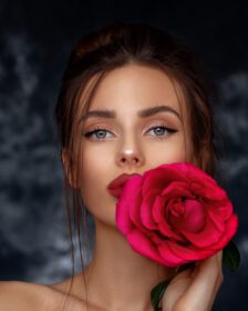 دانلود عکس مدل زیبا در دست گرفتن یک گل رز قرمز بزرگ در پس زمینه قدیمی