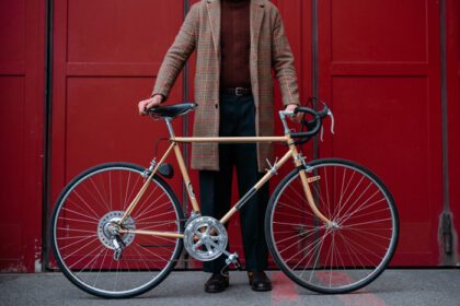 دانلود عکس تاجر جوان با دوچرخه روی پس زمینه دیوار قرمز در الف