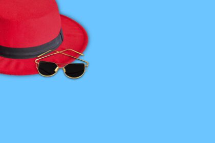 دانلود عکس کلاه قرمزی عینک آفتابی قهوه ای مشکی در پس زمینه آبی تابستان