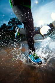 دانلود عکس دونده تکی در حال دویدن در باران و ایجاد آب و هوا در گودال