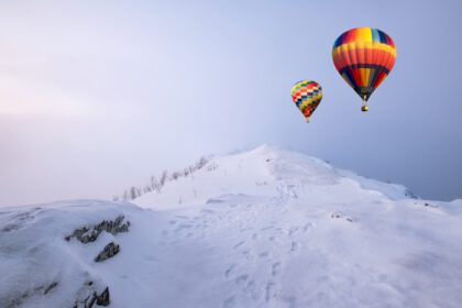 دانلود عکس بالون های رنگارنگ هوای گرم در حال پرواز بر روی تپه برفی همراه با کولاک