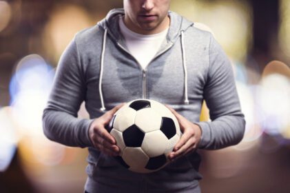 دانلود عکس ورزشکار جوان در شهر شبانه که توپ فوتبال در دست دارد